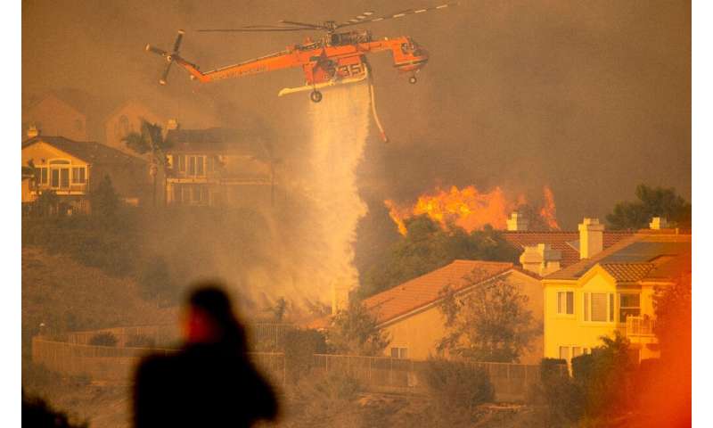 A helicopter drops water to help fight flames as the Saddleridge Fire in the Porter Ranch section of Los Angeles, California on 