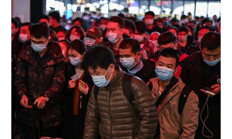 穿着面部面具的乘客在武汉的主要火车站前往他们的火车