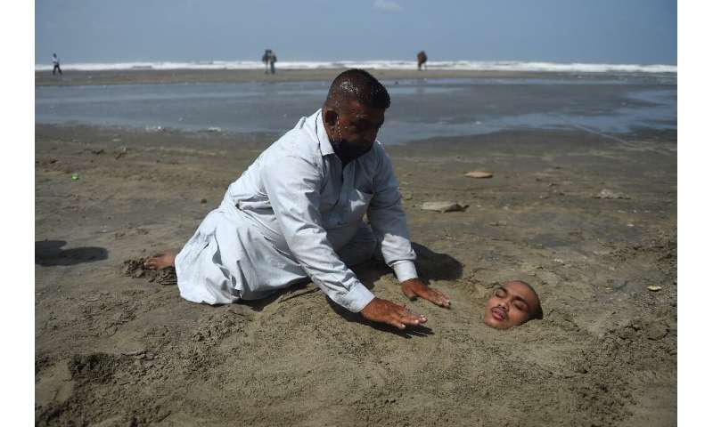 A man buries his paralysed son in sand on a beach in Karachi during the eclipse. Folklore has it if the eclipse passes over them