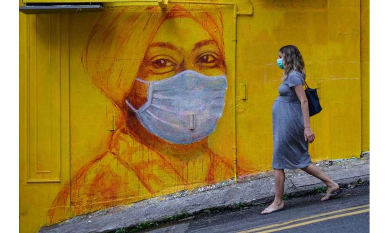 A pregnant woman wearing a face mask as a precautionary measure walks past a street mural in Hong Kong