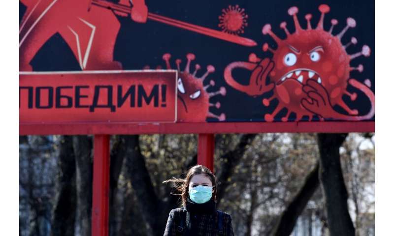A woman wearing a face mask walks past a sign depicting a virus in Minsk