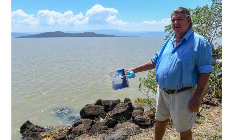 Murray Roberts, 69, holds an old photo of his sons jumping off a cliff face into the lake from the edge where he is standing tha