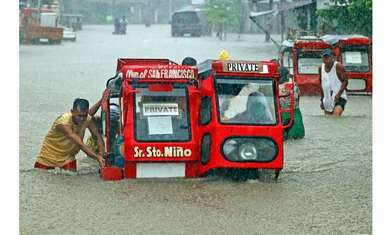 People push a half-submerged tricycle through a flooded street in Agusan del Sur province in Mindanao