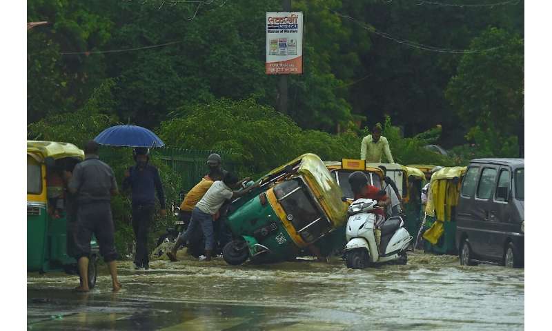 People try to pull an overturned auto rickshaw along a waterlogged road following monsoon rain in New Delhi
