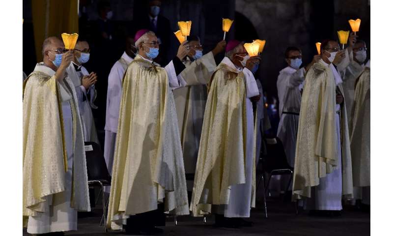 戴着口罩的高级教士手持蜡烛，参加在法国奥古斯的卢德神殿举行的第147次升天朝圣弥撒
