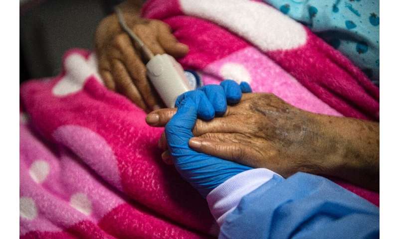 A health worker holds the hand of a Covid patient in Peru. Health experts say that taming the pandemic over the next year is pos