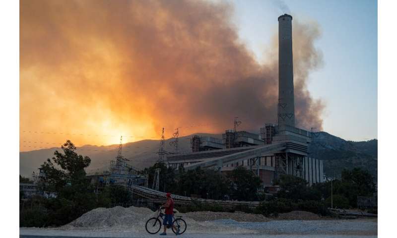 A man pushes a bike along a road in the vicinity of a forest fire close to the Kemerkoy Thermal Power Plant in northen Turkey
