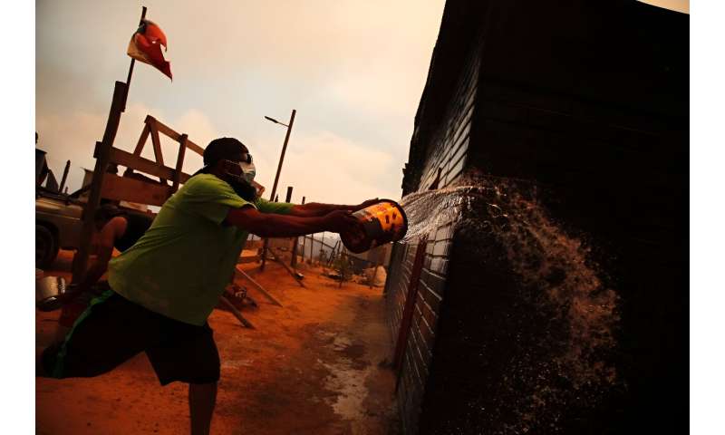 A man douses a burned building with water in Quilpe, where wildfires blazed through the night