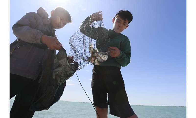 Boys fish near a copper plant which is discharging industrial waste into a body of water right next to the lake