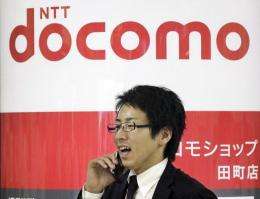 A businessman uses his mobile phone as he passes before the logo of Japanese mobile communication NTT Docomo