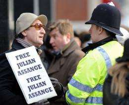 A protester holds a placard reading, "Free Julian Assange" as he talks to a police officer