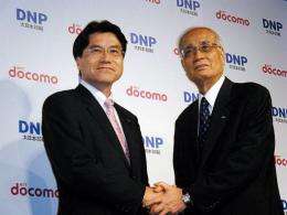 Japan's NTT DoCoMo's Kiyoyuki Tsujimura (L) shakes hands with Japan's Dai Nippon Printing's Koichi Takanami