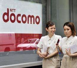 Pedestrians use their mobile phones as they walk past a NTT docomo shop
