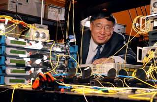 Research Gee-Kung Chang poses with telecommunications equipment used to demonstrate a hybrid wired-wireless network