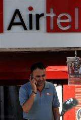 An Indian man talks on his mobile phone next to a Bharti Airtel sign in New Delhi