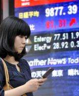 A woman uses her mobile phone near a share prices board in Tokyo