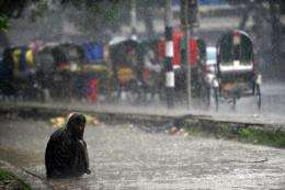 A Bangladeshi homeless man sits on the side of a road during a seasonal rainfall in Dhaka in May