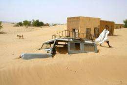 A man walks by a car covered by sand in the village of Boumdeid, near Kiffa in Mauritania, in 2002