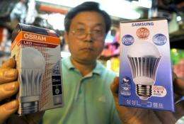 A South Korean worker holds up a Samsung light emitting diode (LED) bulb (R) and an Osram LED bulb (L)