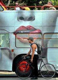 A cyclist waits at an intersection next to a tour bus bearing an advertisement in Los Angeles, California