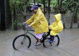 A man cycles across a flooded street with a child in La Libertad, El Salvador