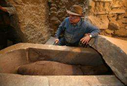 An archaeoligst inspects an Egyptian sarcophagus containing a mummy