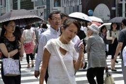 A pedestrian (C) uses a handkerchief to wipe her brow in very hot weather in Tokyo