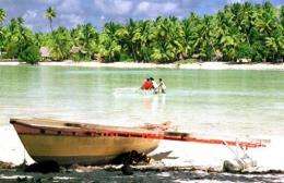 A traditional Micronesian canoe sits on the shore as people cross a lagoon on an atoll of Tarawa