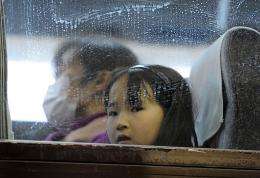 A young girl looks out from a bus window as people rush to get out of the city in Yamagata