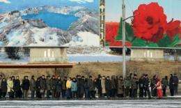 North Korean commuters wait for a bus beneath posters showing Mount Paekdu in Pyongyang