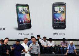People stand under an advertisement showing HTC smartphones in Taipei in April