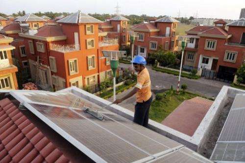 An Indian worker cleans solar panels fitted onto the roof of a residential house in Rabirashmi Abasan