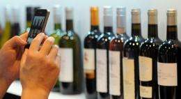 A visitor takes pictures of various bottles of red and white wine with his smartphone