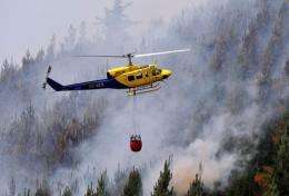 A helicopter carries a water bag to fight a massive forest fire affecting the commune of Ranquil