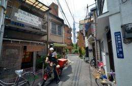A postman drives a motorcycle through a narrow alley to deliver mail in Tokyo's Sumida district