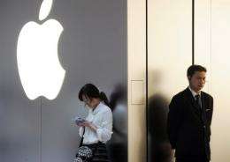 A woman (L) uses her mobile phone as a security guard looks on outside an Apple store in Shanghai