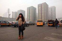 A woman talks on a mobile phone as she stands on a roadside before high-rise apartments in Beijing