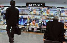 Customers watch televisions under a Sharp logo at an electrical shop in Tokyo