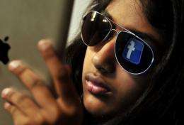 The 'Facebook' logo is reflected in a young Indian woman's sunglasses as she browses on a tablet