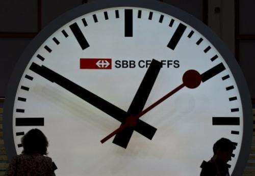 Visitors are silhouetted against a giant railway clock at the Swiss railway