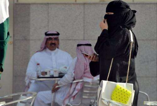 A woman holds a mobile as she walks past a coffee shop in the Saudi capital Riyadh on June 17, 2013