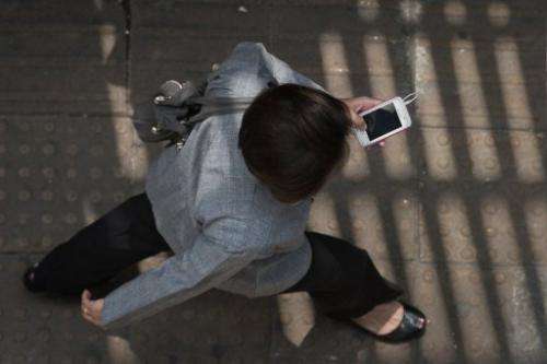 A woman uses her smartphone while walking in a street in Bangkok, March 20, 2013