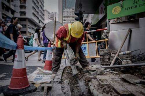A worker uses a pneumatic drill on the pavement as pedestrians walk past in Hong Kong on July 9, 2013
