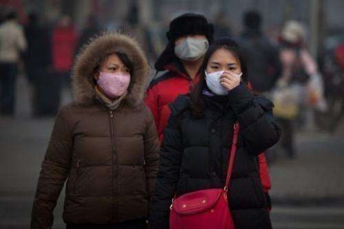 Pedestrians wearing masks wait to cross a road in severe pollution in Beijing on January 12, 2013