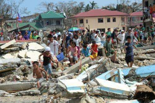 Residents walk through debris as they rush to a rescue helicopter delivering relief foods in Hernani town, Eastern Samar provinc