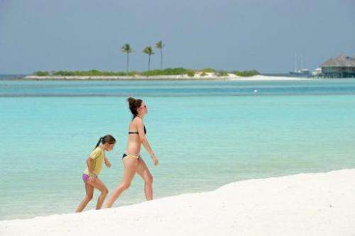 Tourists walk along a beach of the Paradise Island Resort and Spa in the Maldives on February 14, 2012