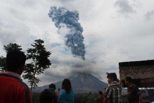 Local residents watch as a giant plume of steam and ash rise and hot lava rolls from the crater of Mount Sinabung volcano, durin