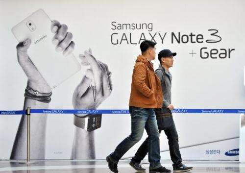Pedestrians walk past a sign board advertising Samsung Electronics' Galaxy Note 3 smartphone at a railway station in Seoul on Oc