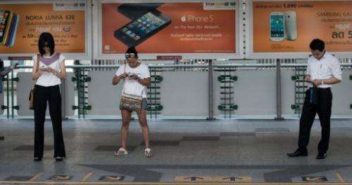 People look at their smartphones while waiting for a train at a BTS station in Bangkok, March 20, 2013