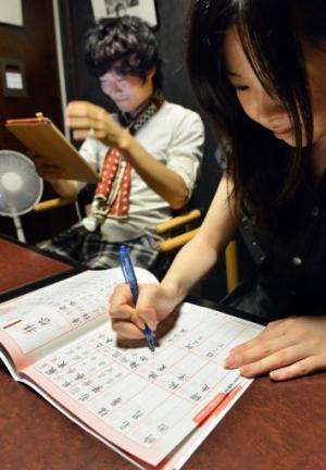 Akihiro Matsumura (L) uses a computer as his friend practices writing Chinese characters in Tokyo on June 19, 2013